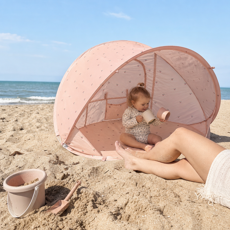 Barn sidder i skyggen i pop up UV-strandtelt i Cherry
